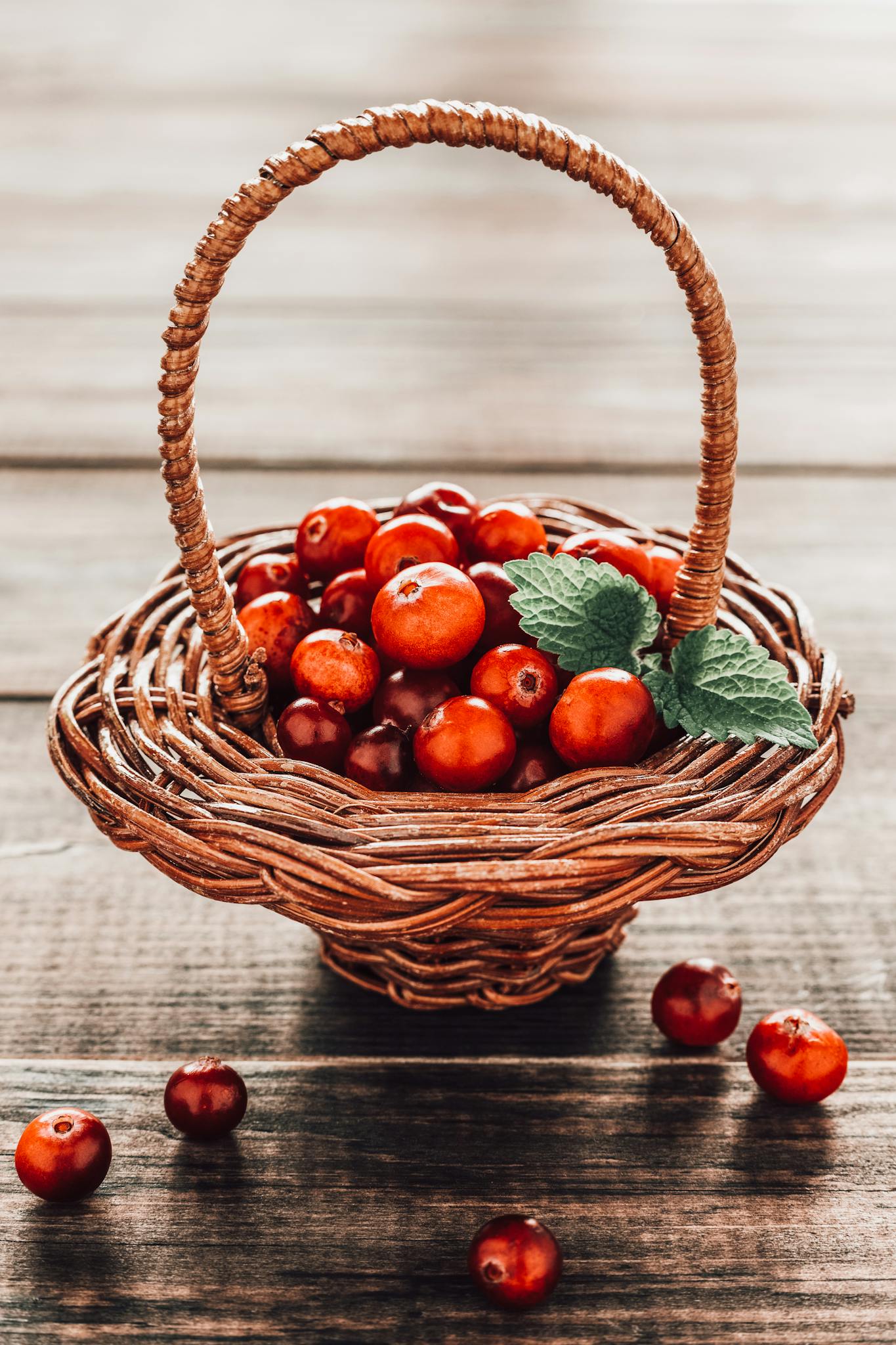 A charming display of ripe cranberries in a rustic woven basket on a wooden surface.